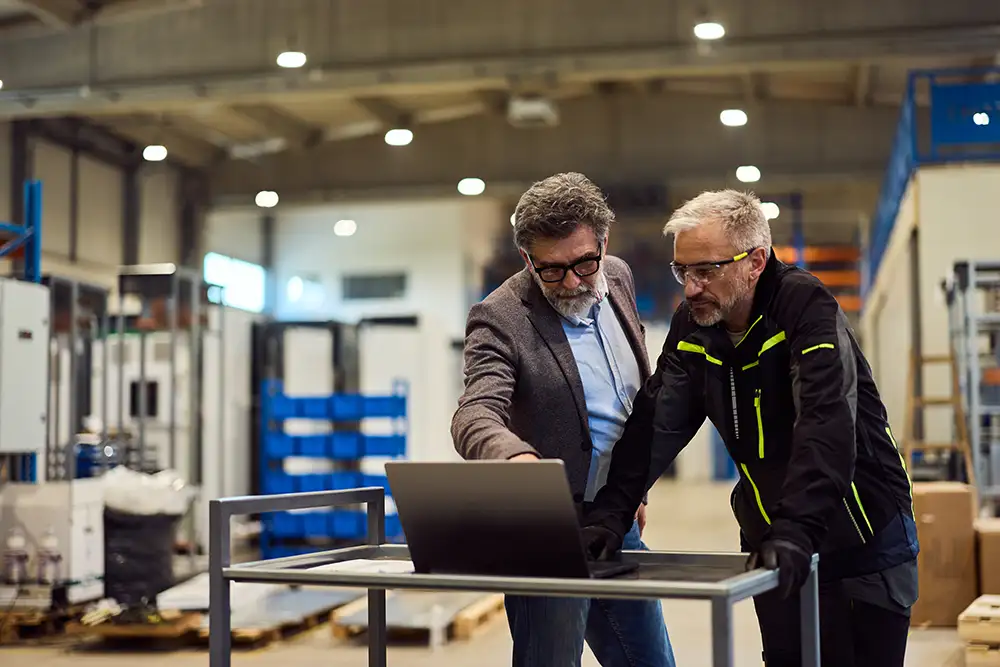 Manager and floor worker reviewing laptop together for PO approval workflow