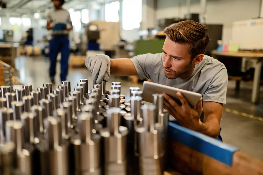 Steel worker inspecting machined parts with tablet for exception monitoring